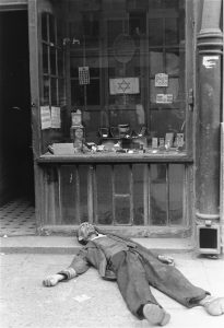 A man lies dead in front of a shop in the Warsaw ghetto in Nazi-occupied Poland, circa June-August, 1941. Photo credit: USHMM #20614