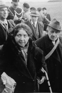An elderly Jewish couple on their way from Hooghalen to the Westerbork transit camp in Holland. A member of the Dutch constabulary stands behind them, October 1942. Photo credit: USHMM #77659