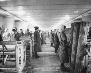 Female Romani forced laborers stand at attention during an inspection of the weaving mill in the Ravensbrück concentration camp in Germany, circa 1943. Photo credit: USHMM, Bildarchiv Preussischer Kulturbesitz