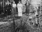 Four female prisoners stand outside a barracks behind a barbed-wire fence in 