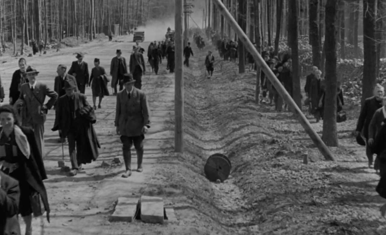 Screenshot from documentary film showing civilians walking in the woods overseen by military personnel circa April 1945